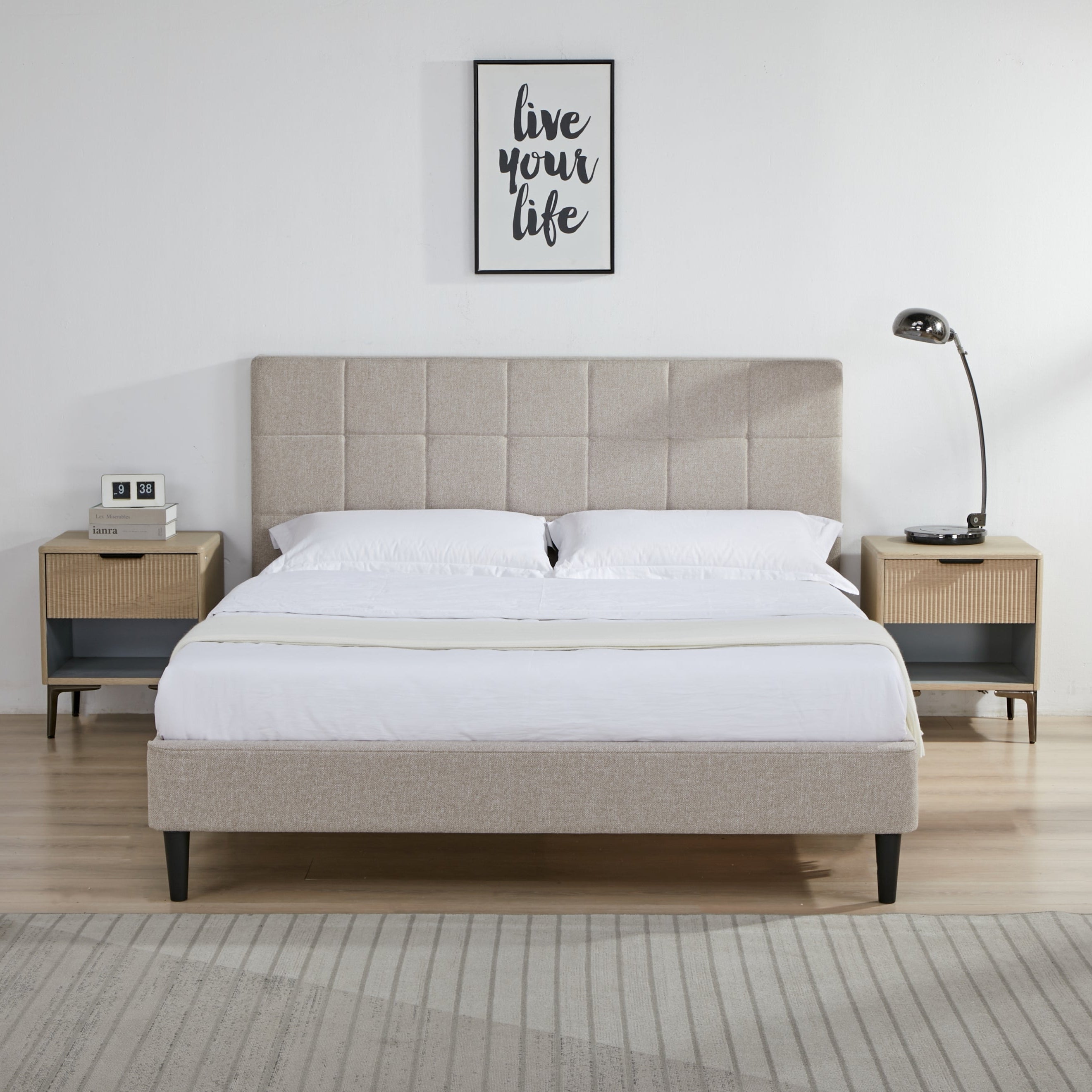 Beige upholstered bed with matching nightstands and a lamp in a bedroom setting.