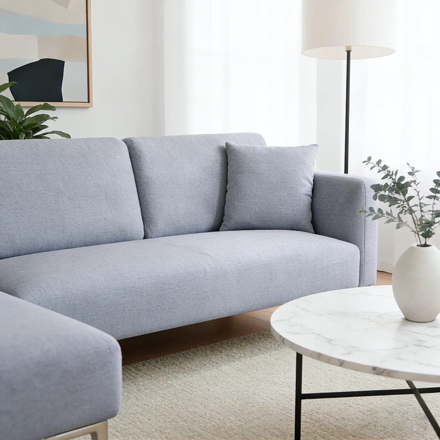 Gray sectional sofa in a living room with a marble coffee table and plants.